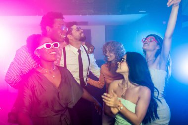 Renkli ışıklar ve enerjik bir atmosferle çevrili canlı bir disko partisinde neşeli bir şekilde dans eden mutlu çoklu etnik arkadaşlar.