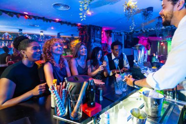 Bir grup neşeli arkadaş eğleniyor, kokteyl içiyor ve barmenle canlı bir barda sosyalleşiyorlar.