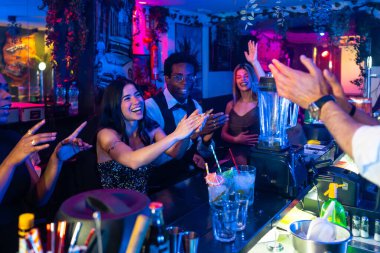 Neşeli çoklu etnik arkadaşlar coşkulu kokteylleri alkışlıyor ve eğleniyorlar, neşeli bir gece atmosferinde kahkaha ve heyecan paylaşıyorlar.