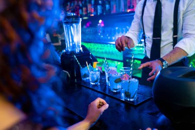 Barmen, canlı bir gece kulübü atmosferinde taze nane ve buzla süslenmiş canlı mavi kokteylleri ustaca hazırlıyor.