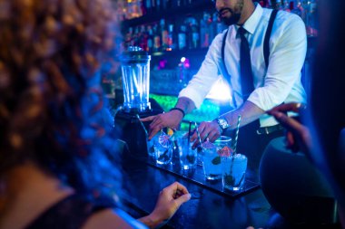 Profesyonel barmen, gece kulübündeki bar tezgahında taze malzemeler ve süslemeler kullanarak kokteyl hazırlıyor.