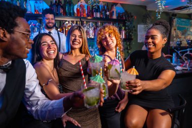 Neşeli bir arkadaş grubu mojito kokteyli kaldırıyor, canlı bir barda gece hayatının tadını çıkarıyor.