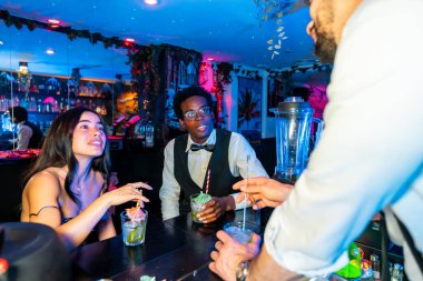 Genç yetişkinler canlı, tropikal bir barda kokteyl içip eğleniyorlar. Canlı ve şenlikli bir ortam yaratıyorlar.