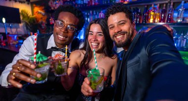 Neşeli çoklu etnik arkadaşlar neşeli bir selfie çekerken aynı zamanda canlı bir gece kulübünde renkli kokteyllerin tadını çıkarıyor, gece hayatını kucaklıyor.