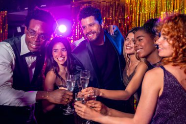 Mutlu çoklu etnik arkadaşlar yeni yıl arifesini kutluyor, görkemli bir partide şampanya kadehleriyle kadeh kaldırıyorlar.