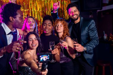 Neşeli çoklu etnik arkadaşlar bir gece kulübünde selfie çekiyorlar ellerinde şampanya kadehleri, gece hayatının tadını çıkarıyorlar.