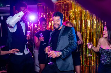 Neşeli genç yetişkinler dans ediyor ve şampanya içiyor, gece klübü partisinde eğleniyor renkli ışıklar ve altın renkli arkaplanlarla