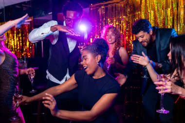 Neşeli çoklu etnik arkadaşlar dans ediyor ve şampanya içiyor, gece kulübünde hayat dolu gece hayatının tadını çıkarıyor.