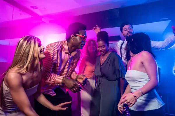 Mutlu çoklu etnik arkadaşlar dans ediyor ve neon ışıklı gece klübünde eğleniyor.