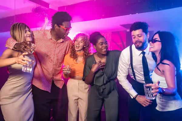 Genç insanlar, renkli ışıklar ve şenlikli konfetiyle çevrili canlı bir gece kulübünün partisinde gülüp eğleniyorlar.