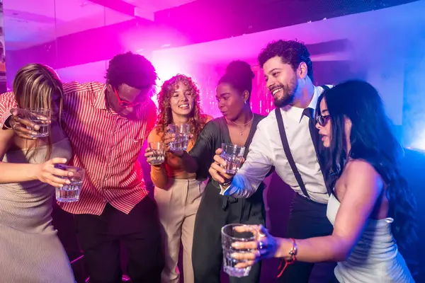 Neşeli çoklu etnik arkadaşlar neon ışıklı gece kulübü partisinde birlikte içki içiyorlar.