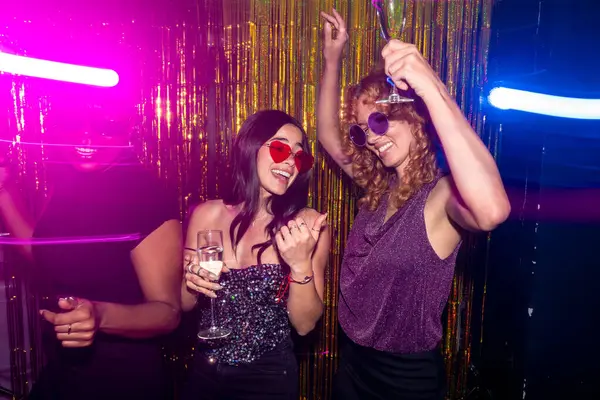 Disko partisinde dans eden ve köpüklü şarap içen üç neşeli kadın.