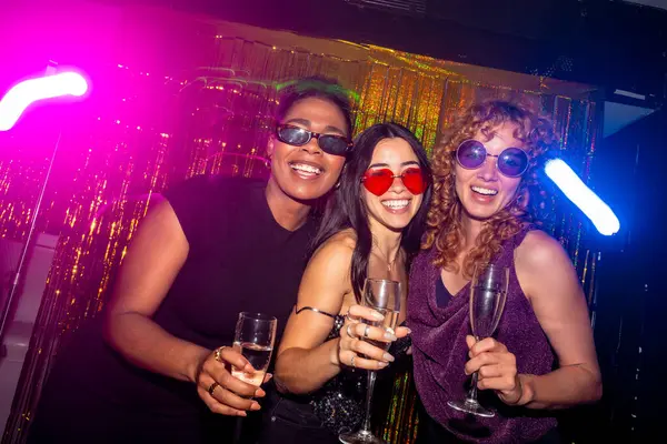 Üç çok ırklı bayan arkadaş, renkli neon ışıklarla dolu canlı bir gece kulübünde içki içip kutlama yapıyorlar.