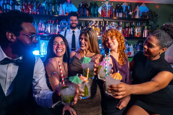 Neşeli çoklu etnik arkadaşlar bir gece kulübünde kadeh kaldırmak için kokteyl kadehleri kaldırıyor. Barmenin arka planında gece hayatının tadını çıkarıyorlar.