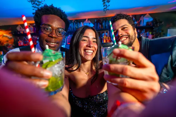 Neşeli çoklu etnik arkadaşlar canlı bir barda kokteyl içip hafta sonu gece hayatını kutluyorlar.
