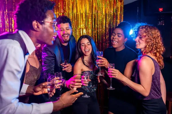 Bir grup neşeli çoklu etnik arkadaş şampanya bardaklarıyla kadeh kaldırıyor, gece hayatının tadını çıkarıyor ve gece kulübünde birlikte kutluyorlar.