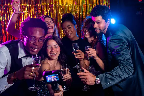 Bir grup neşeli çoklu etnik arkadaş fotoğraf makinesiyle selfie çekerken gece kulübü partisinde altın arkaplanlı şampanya kadehlerinin keyfini çıkarıyorlar.