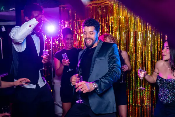 Neşeli genç yetişkinler dans ediyor ve şampanya içiyor, gece klübü partisinde eğleniyor renkli ışıklar ve altın renkli arkaplanlarla