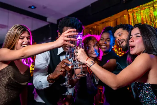 Neşeli çoklu etnik arkadaşlar şampanya kadehleri tokuşturuyor, gece kulübü partisinde birlikte kutlama yapıyorlar.