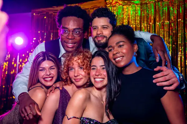 Bir grup neşeli zarif arkadaş, gece kulübü partisinde fotoğraf çektirmek için birlikte poz veriyorlar. Disko ışıkları ve altın renkli perdelerle.