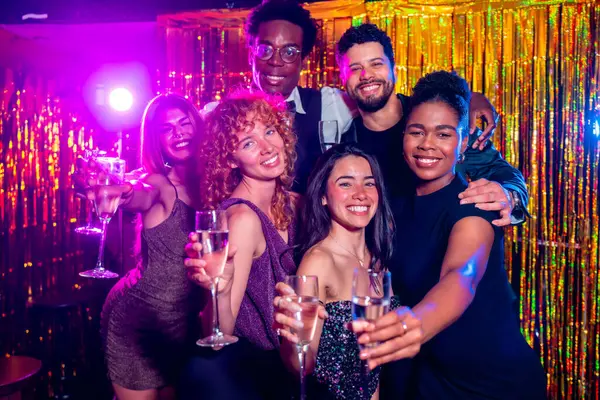 Bir grup neşeli zarif arkadaş şampanya kadehleri tokuşturuyor, gece hayatının tadını çıkarıyorlar altın arka planda bir gece kulübü partisinde.