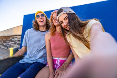 Üç neşeli patenci mavi bir duvara karşı selfie çekiyorlar, günlerinin anılarını yakalıyorlar.