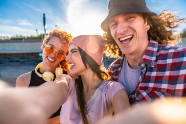 Üç neşeli genç arkadaş dışarıda selfie çekiyorlar, güneşleniyorlar ve şehirde canlı bir günün tadını çıkarıyorlar.
