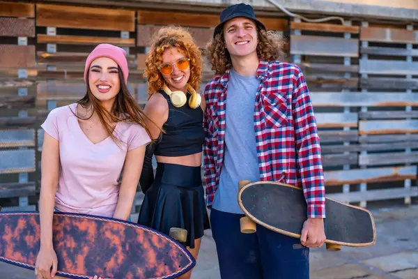 Bir grup neşeli arkadaş kaykay parkında eğleniyor. Kadın ve erkek patenciler ellerinde sörf tahtalarıyla, pozitif şehir yaşam tarzlarını ifade ediyorlar.