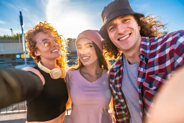 Üç neşeli arkadaş dışarıda selfie çekiyorlar, batan güneşin sıcacık parıltısının tadını çıkarıyorlar.