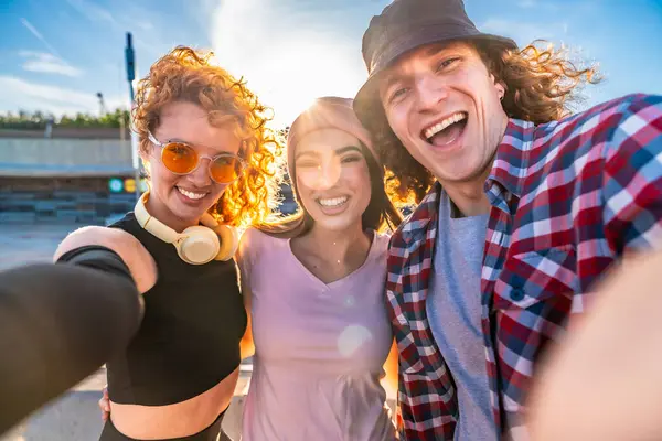 Kıvırcık saçlı üç neşeli arkadaş açık havada neşeli bir an yakalıyorlar, gülücükler ve arkadaşlıkla güneşin tadını çıkarıyorlar.