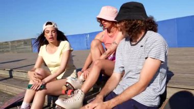 Paten giyen bir grup arkadaş, güneşli bir günde tahta merdivenlerde oturup sohbet ediyorlar.