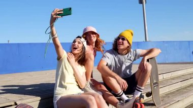 Gen z arkadaşları canlı yaz anlarını yakalıyor, selfie çekiyorlar ve kaykay arkadaşlığının tadını çıkarıyorlar açık mavi gökyüzü altında kentsel eğlence alanında.