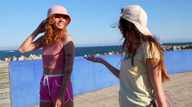 Kaykaylı iki bayan arkadaş deniz kenarında güneşli bir günün tadını çıkarıyor, sohbet ediyor ve birlikte gülüyorlar.
