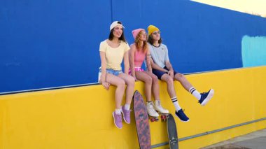 Bir grup şık arkadaş canlı bir duvarda takılıp kaykaylarını ve gençlik enerjilerini sergiliyorlar.
