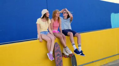 Renkli bir duvarda kaykay ve paten ile poz veren bir grup şık arkadaş, şehir atmosferinin tadını çıkarıyorlar.