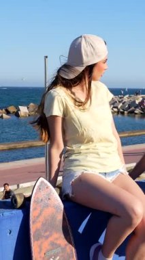 İki arkadaş sohbet eder ve okyanus kıyısında güneşli bir günün tadını çıkarırlar. Kaykaylar gülerken ve sohbet ederken korkuluklara yaslanır.