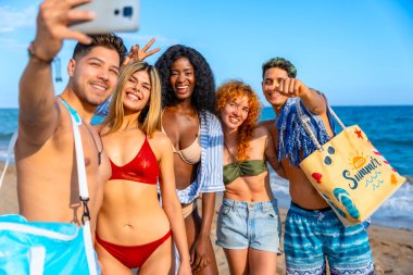 Bir grup neşeli çoklu etnik arkadaş sahilde selfie çekiyorlar, yaz tatillerinin tadını çıkarıyorlar.