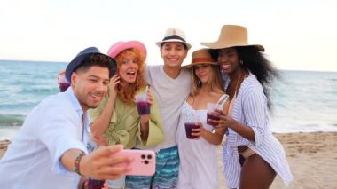 Çok ırklı arkadaşlar plaj tatili anılarını yakalıyor, güneşli sahil anlarında ferahlatıcı kokteyller ve kahkahalar paylaşıyorlar.