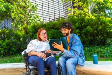 Tekerlekli sandalyedeki mutlu kadın ve erkek birlikte tablet kullanıyor, şehir parkında boş vakitlerin tadını çıkarıyor, kapsayıcılık ve ulaşılabilirlik kavramı
