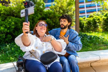 Parktaki bankta oturan iki içerikli yaratıcı akıllı telefon ve telsiz kullanarak video blogu çekiyor.