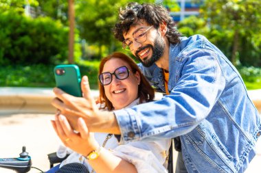 Dışarıda güneşli bir günün tadını çıkaran gülümseyen arkadaşlar, parka dahil olmayı, hareket etmeyi ve arkadaşlığı kutlarken neşeli bir selfie çekiyorlar.