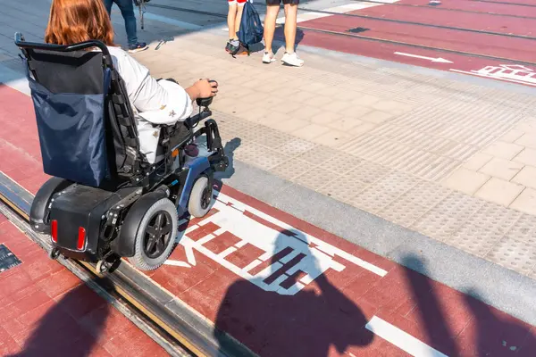 Şehir ortamında belirlenmiş tramvay raylarında tekerlekli sandalyeyle dolaşan bir kadın, ulaşılabilirlik ve kentsel hareketlilik sergiliyor.
