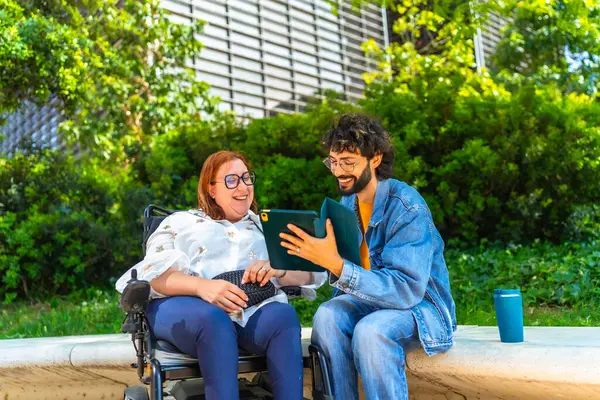 Tekerlekli sandalyedeki mutlu kadın ve erkek birlikte tablet kullanıyor, şehir parkında boş vakitlerin tadını çıkarıyor, kapsayıcılık ve ulaşılabilirlik kavramı