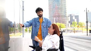 Genç adam, şehirdeki engelli kadına interaktif ekranda bir şey gösteriyor.