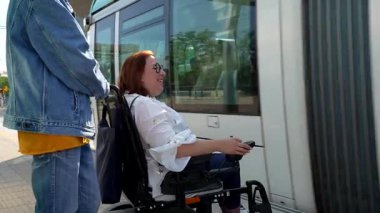 Elektrikli sandalye kullanan mutlu engelli kadın istasyonda tramvay bekliyor, bir arkadaşın yardımıyla.