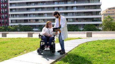 Tıbbi uzman, şehir parkında tekerlekli sandalyedeki engelli kadına tablet hakkında bilgi veriyor.