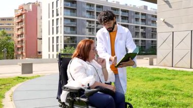 Tıbbi uzman danışmanlığı, açık hava parkı toplantısında tekerlekli sandalye kullanıcısıyla sağlık detaylarını tartışmak, hasta bakımının gösterilmesi ve destekleyici iletişimin sağlanması