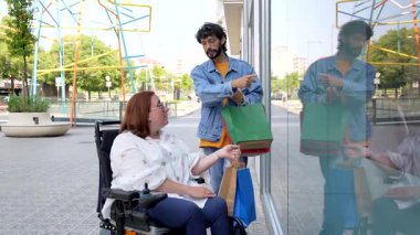 Genç bir adam tekerlekli sandalyedeki engelli bir kadına vitrin gösteriyor. Konuşuyor ve eğleniyor.