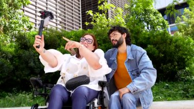 Çeşitli içerik yaratıcıları birlikte çalışırken yardımcı teknolojiyi kullanır, güneşli şehir parkı ortamında sosyal medya içeriği üretir, kapsayıcı modern yaşam tarzını temsil eder