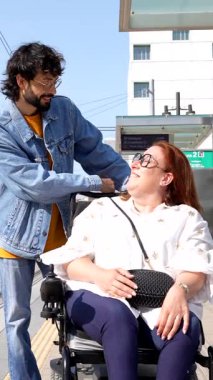 Engelli arkadaşını destekleyen nazik bir adam, toplu taşıma durağında rahatlık ve yardım teklif ediyor.